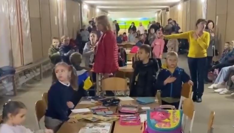 Rusia bombardon Ukrainën, fëmijët të frikësuar këndojnë në kor himnin kombëtar brenda strehimores në Kiev
