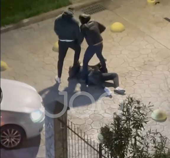 Një person goditet nga dy të tjerë me shkelma kokës teksa është i shtrirë në mes të rrugës